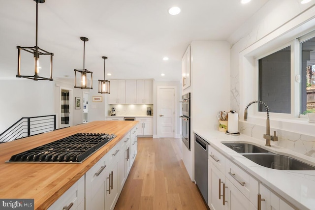 kitchen with light wood finished floors, appliances with stainless steel finishes, white cabinetry, wood counters, and a sink