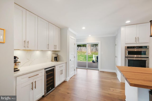 kitchen featuring white cabinetry, stainless steel double oven, wine cooler, butcher block counters, and decorative backsplash