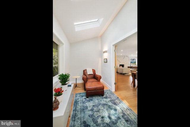 sitting room with baseboards, lofted ceiling with skylight, wood finished floors, and a high end fireplace