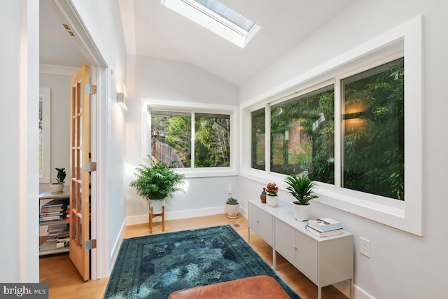 living area featuring light wood finished floors, vaulted ceiling with skylight, and baseboards