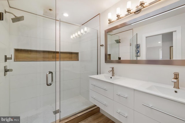 bathroom featuring double vanity, wood finished floors, a stall shower, and a sink