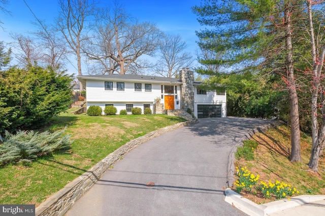 split foyer home with an attached garage, driveway, a chimney, and a front lawn
