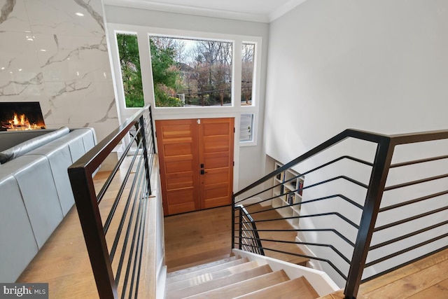 staircase featuring a fireplace, crown molding, and wood finished floors