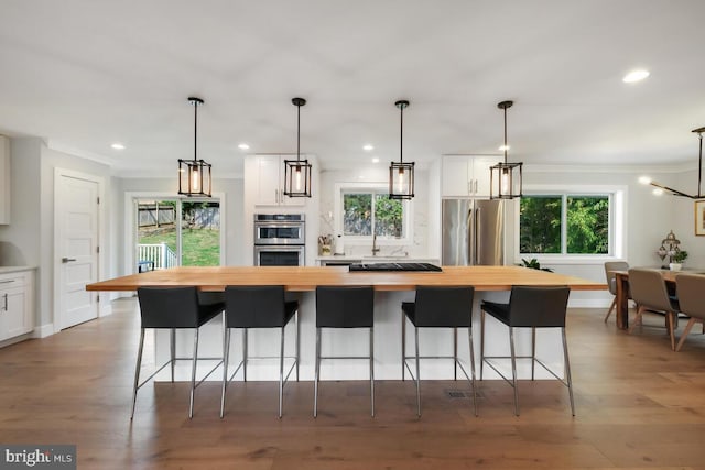 kitchen featuring wood finished floors, wooden counters, a kitchen island, white cabinets, and appliances with stainless steel finishes