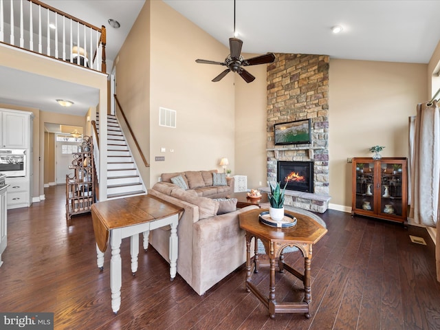 living room featuring visible vents, dark wood finished floors, a stone fireplace, ceiling fan, and stairs