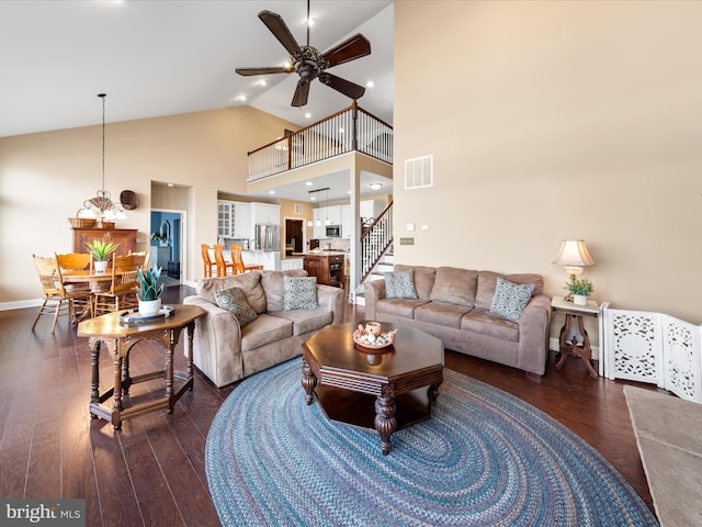 living room with visible vents, baseboards, high vaulted ceiling, dark wood-type flooring, and ceiling fan with notable chandelier