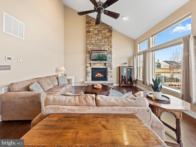 living area featuring visible vents, a stone fireplace, dark wood-type flooring, and a ceiling fan