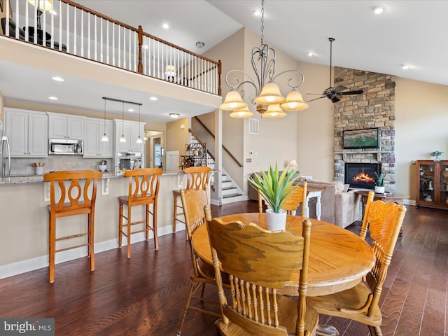 dining space featuring visible vents, high vaulted ceiling, a fireplace, dark wood-type flooring, and ceiling fan with notable chandelier