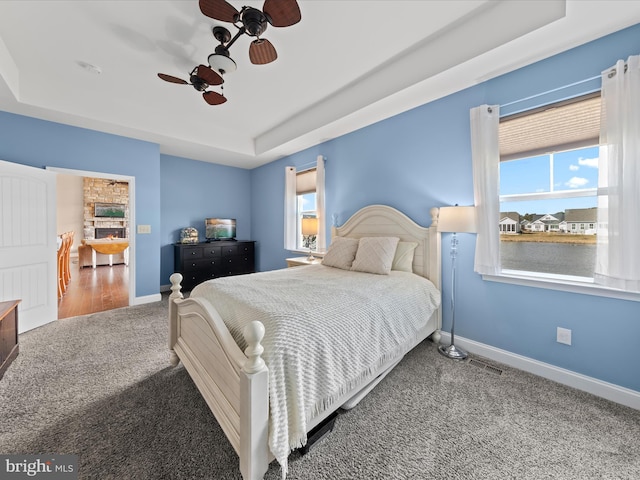 carpeted bedroom featuring a raised ceiling, multiple windows, a ceiling fan, and baseboards
