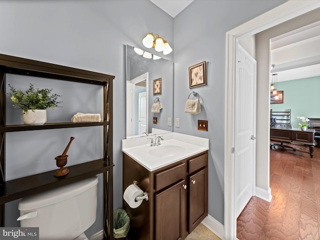 bathroom featuring baseboards, toilet, wood finished floors, and vanity