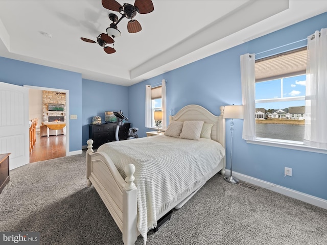 carpeted bedroom with a tray ceiling, multiple windows, baseboards, and a ceiling fan