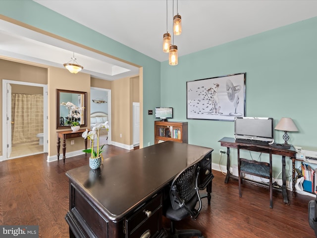 office space featuring a tray ceiling, baseboards, and dark wood-style flooring