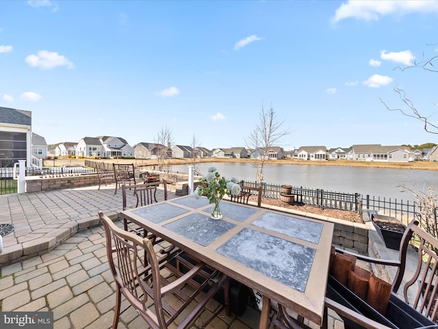 view of patio with a residential view, outdoor dining space, fence, and a water view