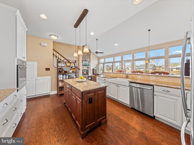 kitchen with a sink, dark wood-style floors, stainless steel appliances, a stone fireplace, and ceiling fan