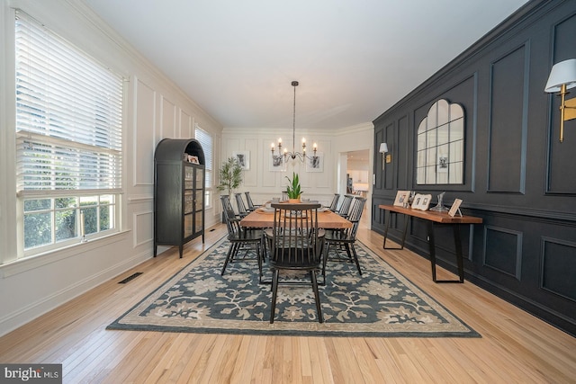 dining space featuring visible vents, ornamental molding, light wood-type flooring, a decorative wall, and a notable chandelier