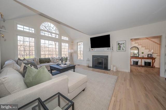 living room with high vaulted ceiling, a fireplace with flush hearth, baseboards, stairs, and light wood finished floors