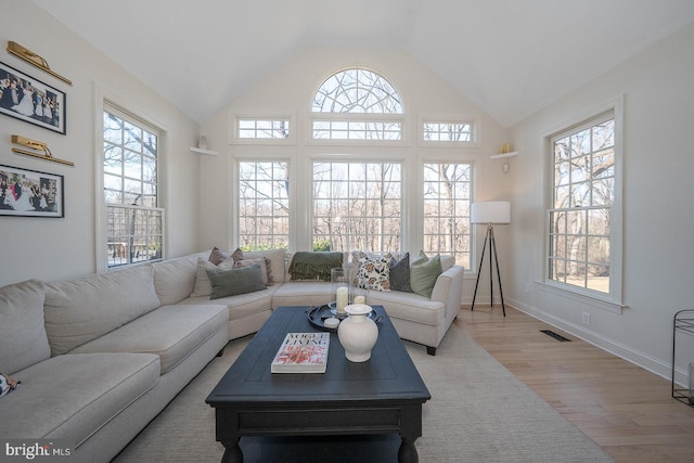 living area featuring high vaulted ceiling, visible vents, baseboards, and wood finished floors