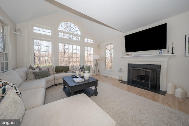 living area with a fireplace with flush hearth, high vaulted ceiling, baseboards, and wood finished floors