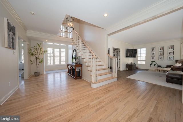 entrance foyer featuring a wealth of natural light, light wood-type flooring, crown molding, and stairs