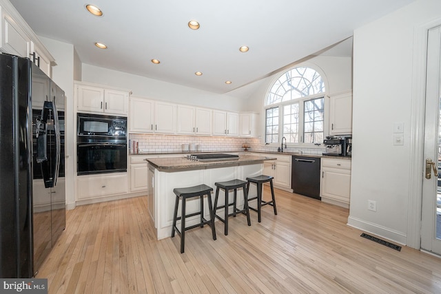 kitchen with a breakfast bar area, a sink, visible vents, black appliances, and tasteful backsplash