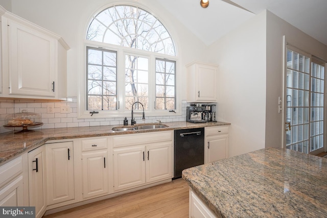 kitchen with light stone counters, black dishwasher, tasteful backsplash, lofted ceiling, and a sink