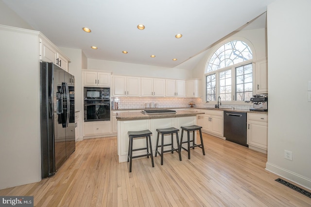 kitchen featuring tasteful backsplash, visible vents, a kitchen island, black appliances, and a sink