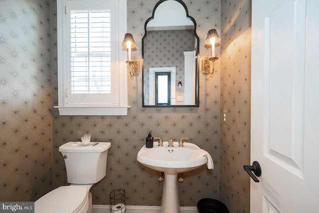 bathroom with a sink, toilet, and wallpapered walls