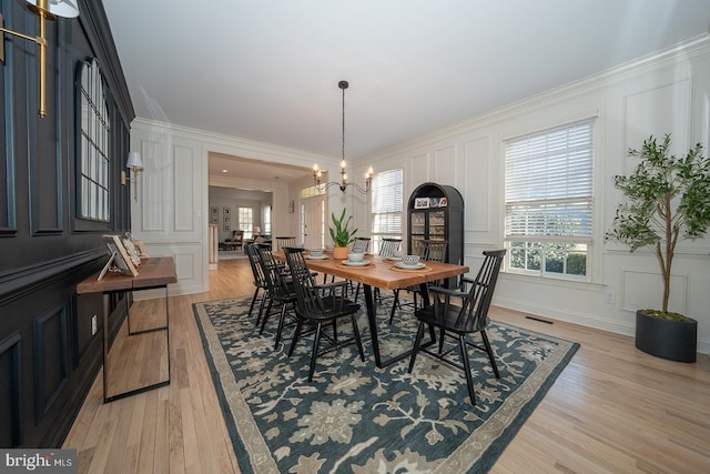 dining area featuring visible vents, a decorative wall, an inviting chandelier, ornamental molding, and light wood-style floors