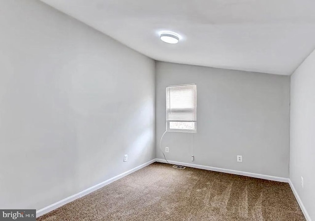 spare room featuring carpet floors, visible vents, vaulted ceiling, and baseboards