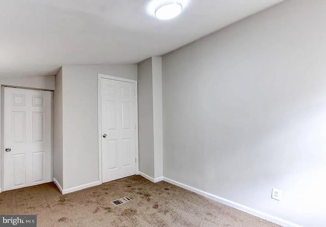 unfurnished bedroom with baseboards, visible vents, vaulted ceiling, and carpet flooring