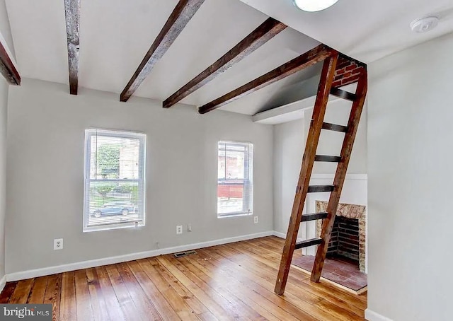 unfurnished living room featuring plenty of natural light, light wood-style flooring, baseboards, and beam ceiling