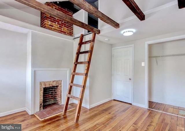 unfurnished living room with wood-type flooring, a fireplace with raised hearth, beamed ceiling, and baseboards