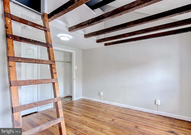 interior space with light wood-style flooring, beam ceiling, and baseboards