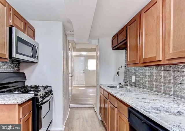 kitchen featuring brown cabinets, decorative backsplash, a sink, light stone countertops, and black appliances