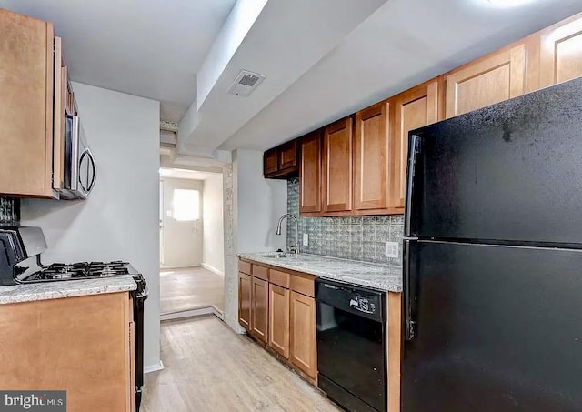 kitchen with visible vents, decorative backsplash, light wood-type flooring, black appliances, and a sink