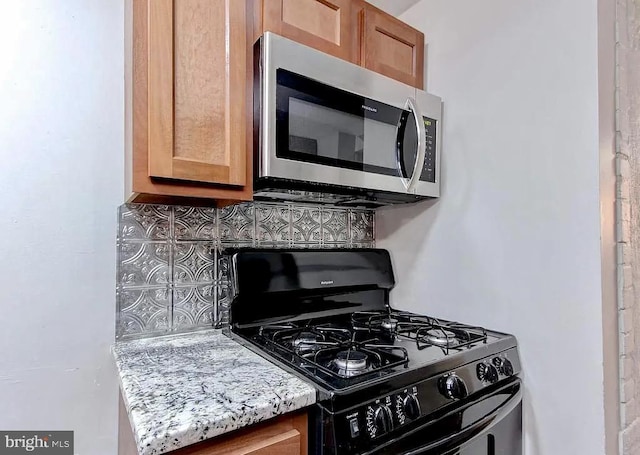 kitchen with stainless steel microwave, decorative backsplash, brown cabinetry, black range with gas cooktop, and light stone countertops