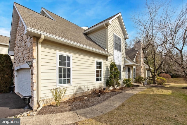 view of side of property with an attached garage, a shingled roof, stone siding, a lawn, and a chimney