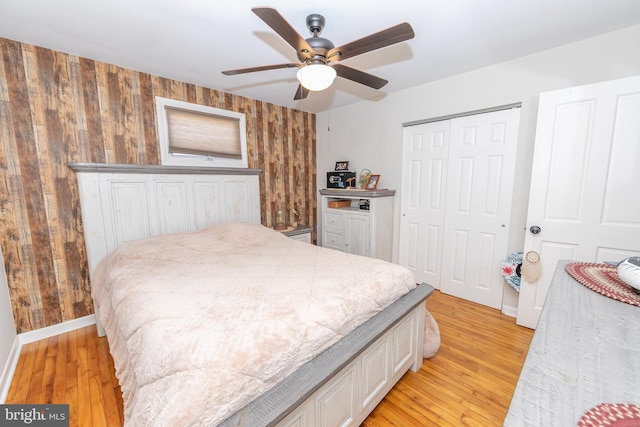 bedroom featuring a closet, light wood-style floors, a ceiling fan, wood walls, and baseboards