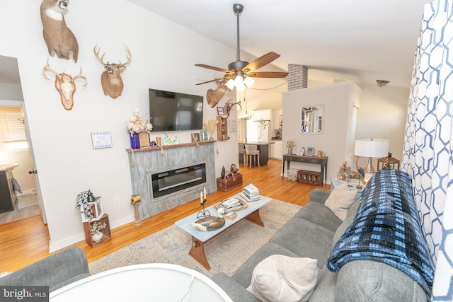 living room with lofted ceiling, wood finished floors, a ceiling fan, baseboards, and a glass covered fireplace