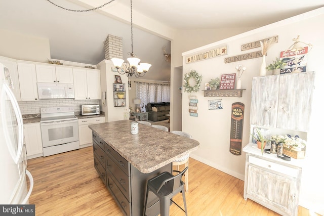 kitchen with vaulted ceiling, white appliances, a kitchen island, and white cabinets