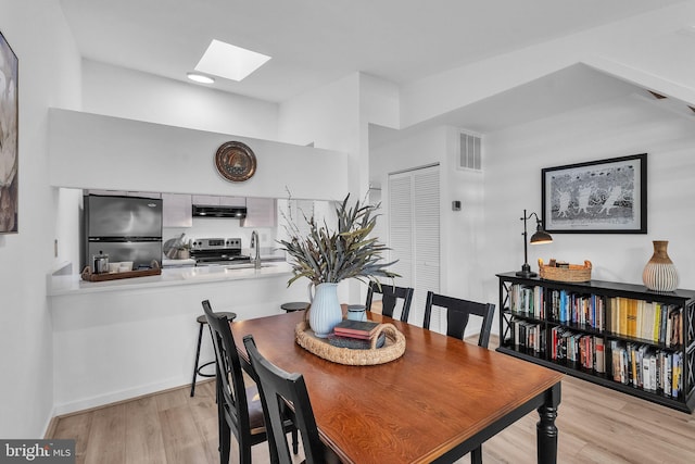 dining area featuring a skylight, baseboards, visible vents, and light wood finished floors