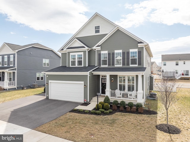 traditional-style house with aphalt driveway, a front yard, covered porch, and a garage