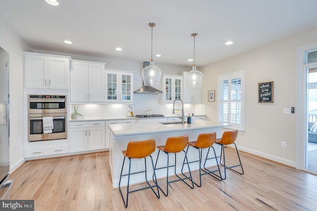 kitchen with wall chimney exhaust hood, a breakfast bar area, a sink, double oven, and backsplash