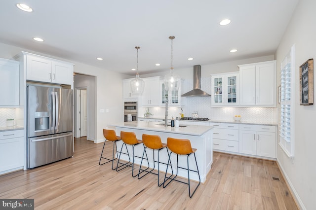 kitchen with light wood-style flooring, stainless steel appliances, white cabinetry, wall chimney range hood, and a kitchen bar