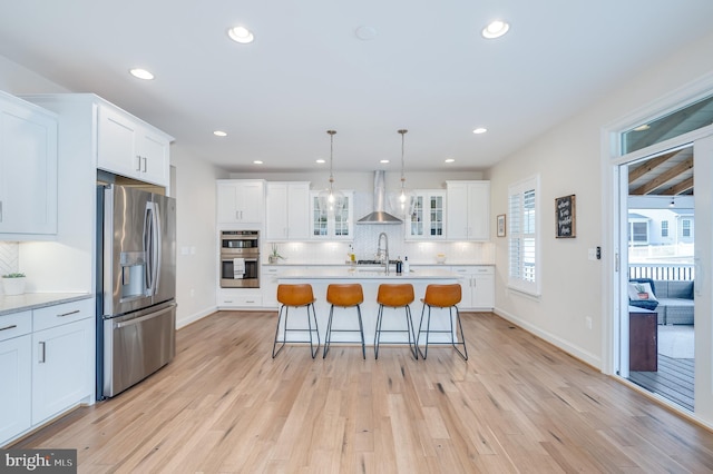 kitchen with stainless steel appliances, wall chimney exhaust hood, light countertops, and light wood-style floors