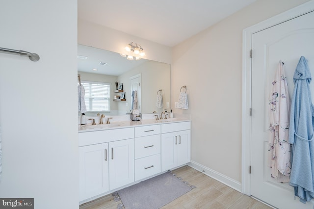 bathroom with double vanity, wood finished floors, a sink, and baseboards