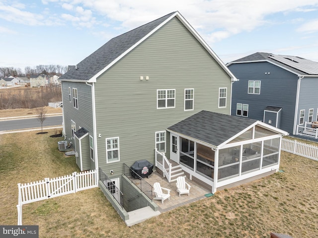 rear view of house with a patio, a fenced backyard, a sunroom, roof with shingles, and a lawn