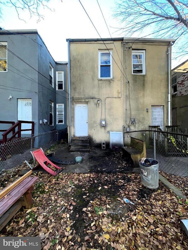 rear view of house featuring entry steps, fence, and stucco siding