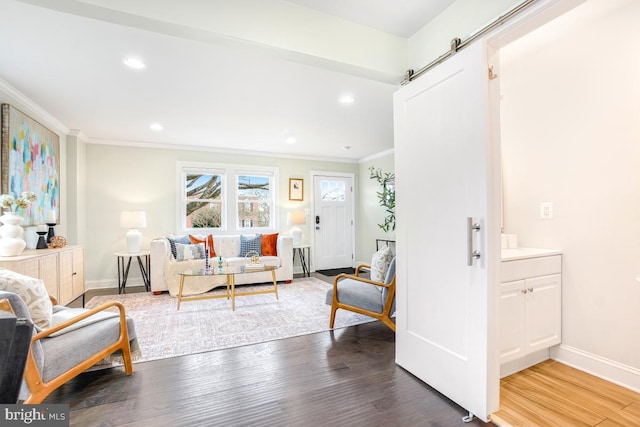 living area featuring a barn door, baseboards, ornamental molding, wood finished floors, and recessed lighting