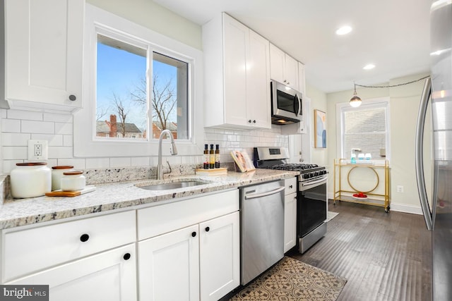 kitchen featuring light stone counters, stainless steel appliances, a sink, white cabinets, and decorative backsplash